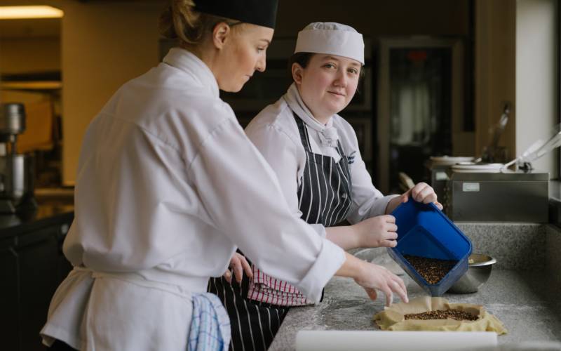 Catering students wearing aprons and hats working in college kitchen