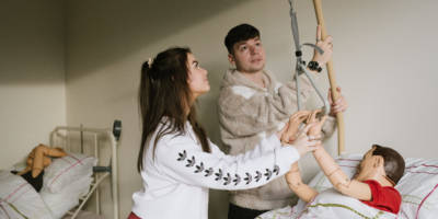 SWC students role-playing using health and care equipment. One student is lying in a bed, while two other are working a hoist.