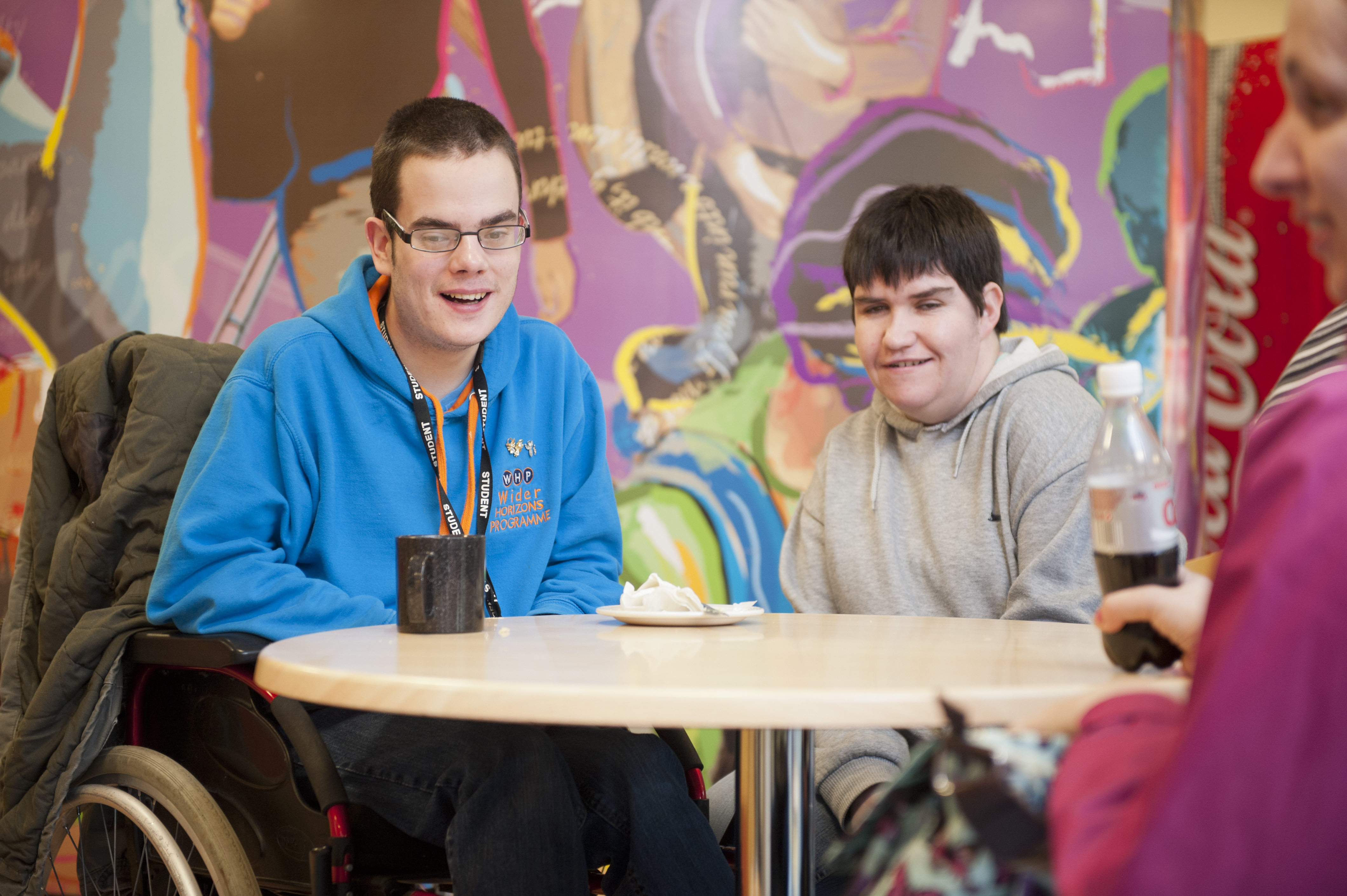 Two South West College students sitting at a table, one is using a wheelchair