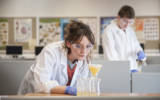 Students in science lab using science equipment and wearing white lab coats
