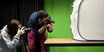 Two South West College students taking photographs in front of a green screen and photography equipment